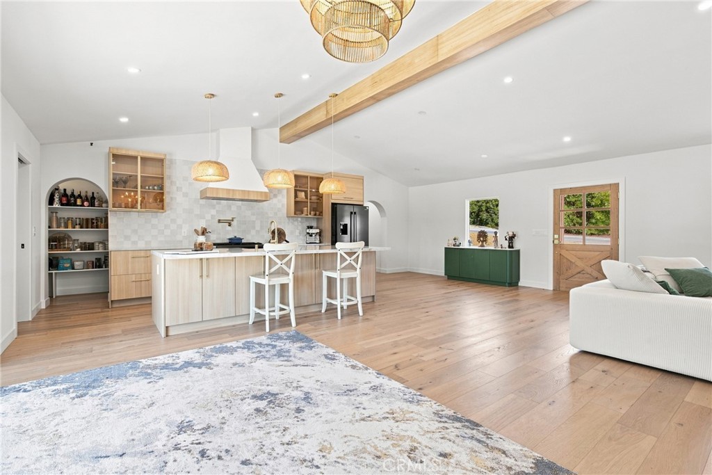Open-plan kitchen and living area with light wood cabinetry, a large island, and woven pendant lights.