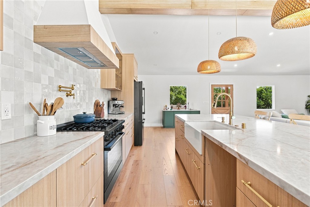 Bright kitchen with light wood cabinetry, marble-look counters, and a large island beneath woven pendant lights.