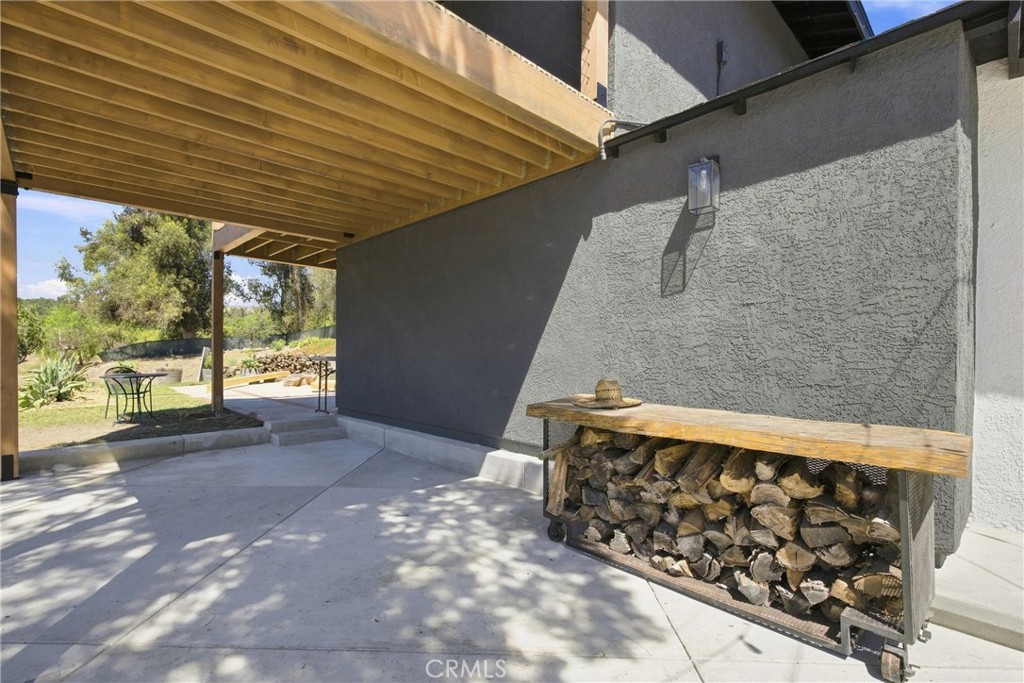Covered patio with exposed wood beams and a firewood rack against a gray stucco wall.