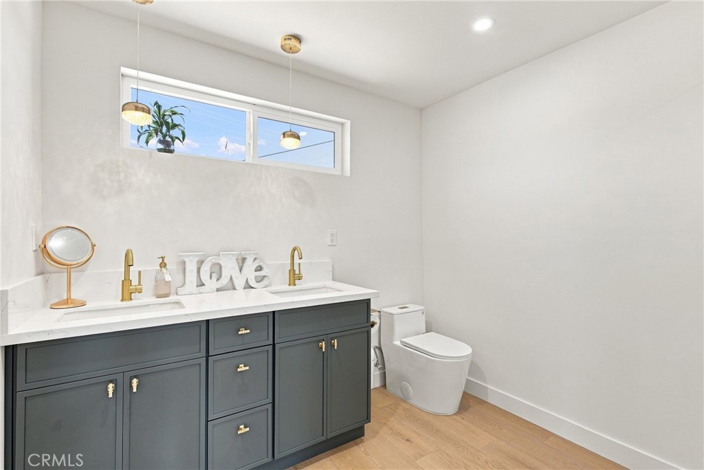 Bathroom with a dark gray double vanity, brass hardware, high windows, and a white toilet.