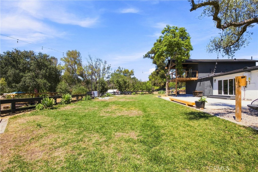 Grassy backyard with mature trees, a dark fence, and a raised wood deck beside the house.