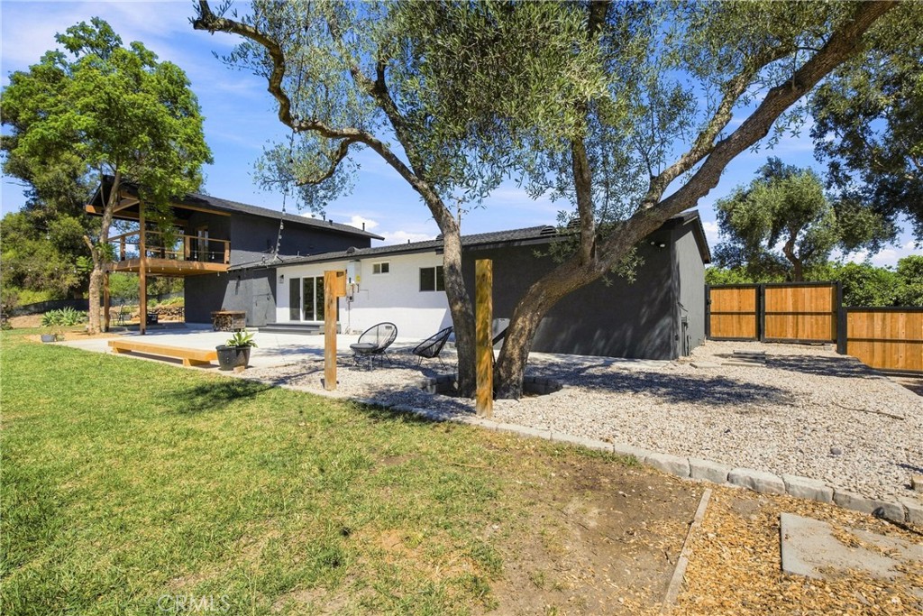 Rear exterior of a modern home with a raised deck, gravel patio, and mature trees.