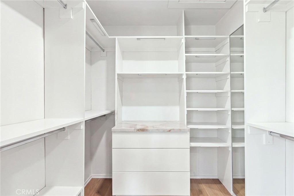 Walk-in closet with white built-ins, a marble-look counter, and wood flooring.