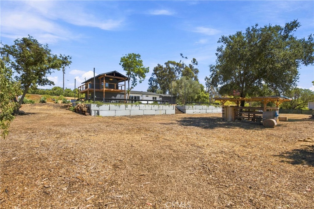 Home and raised deck structure on a spacious dry lot with mature trees and a covered wooden shelter.