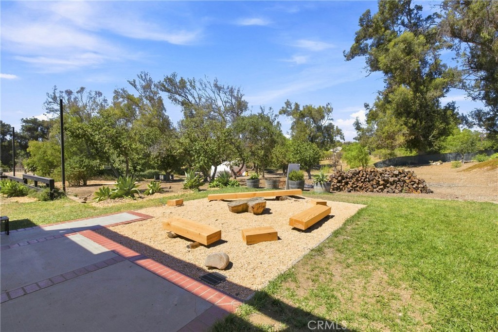 Backyard fire pit area with wooden benches, gravel, and mature trees.