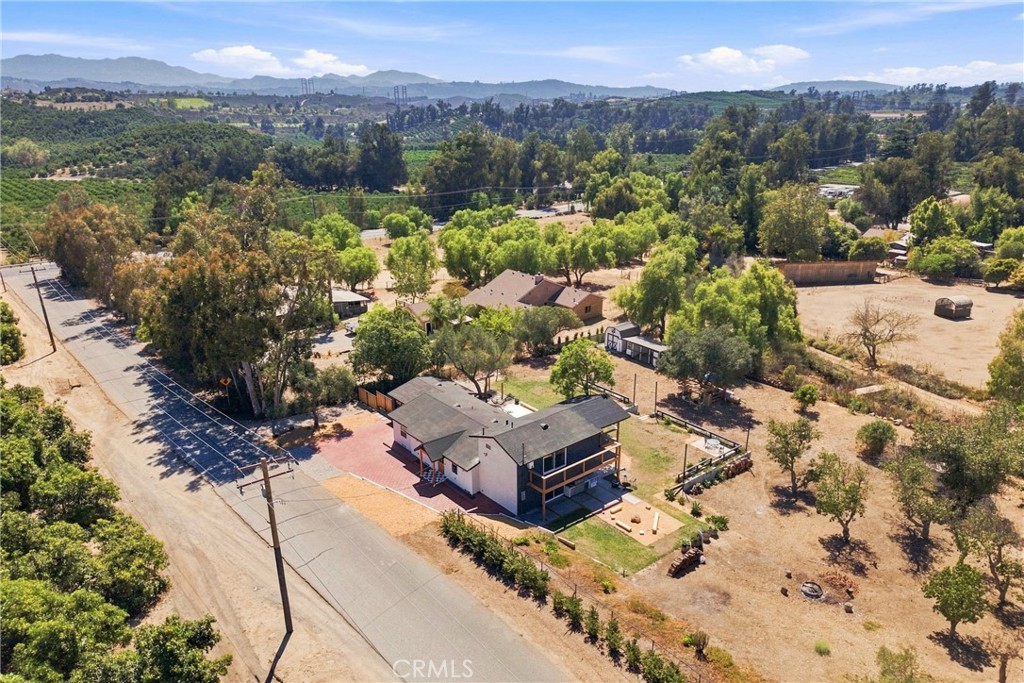 Aerial view of a house on a spacious lot beside a rural road, with hills beyond.