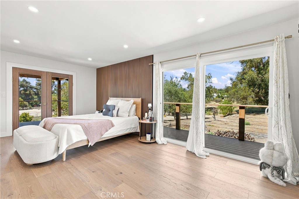 Bedroom with wood-slat accent wall, French doors, and sliding doors opening to a tree-lined deck.