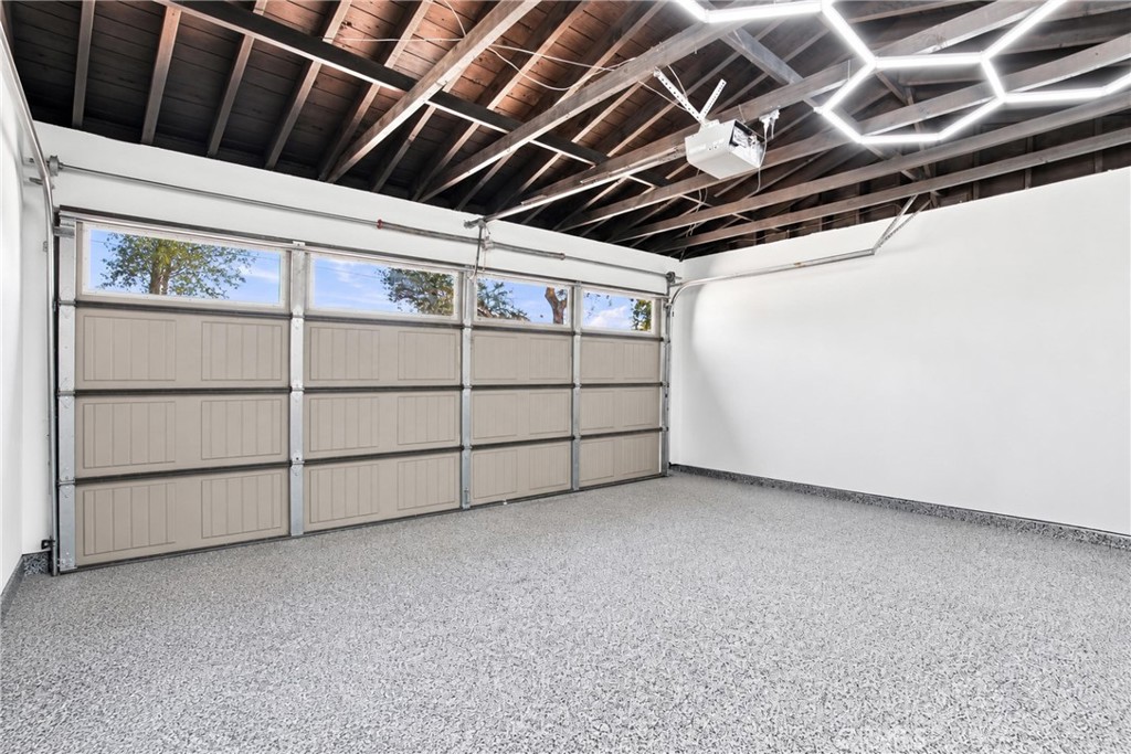 Empty garage with a speckled floor, windowed sectional door, and exposed ceiling beams.