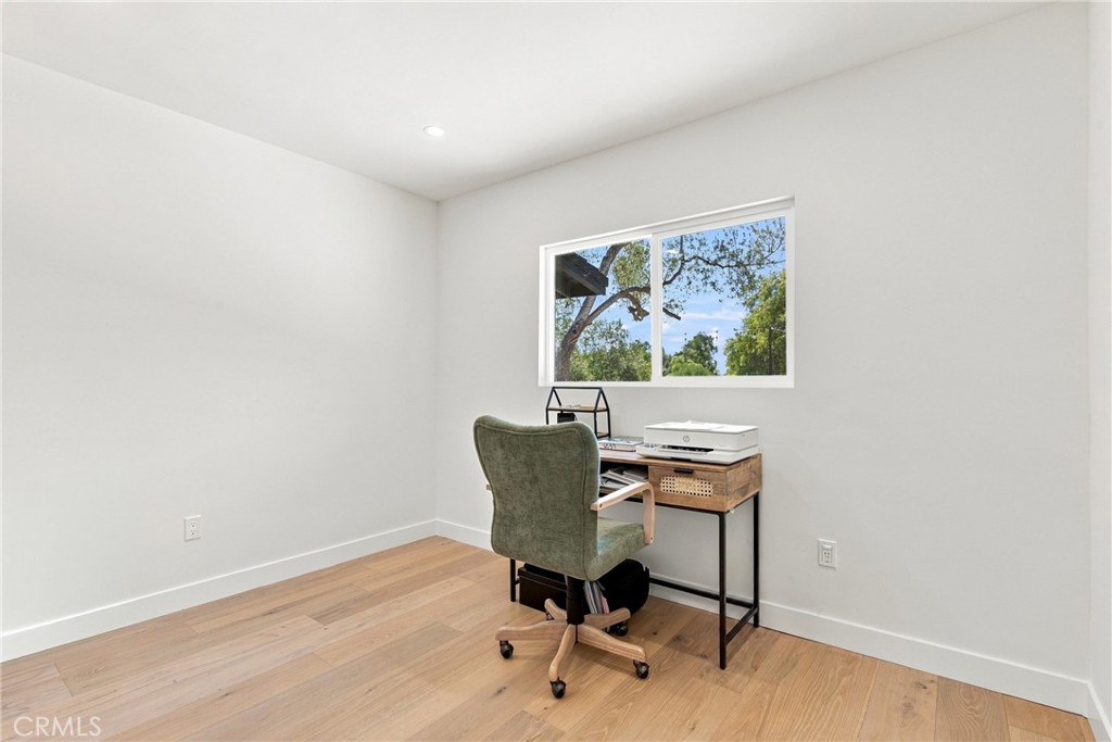 Home office with a desk and green chair beneath a wide window overlooking trees.