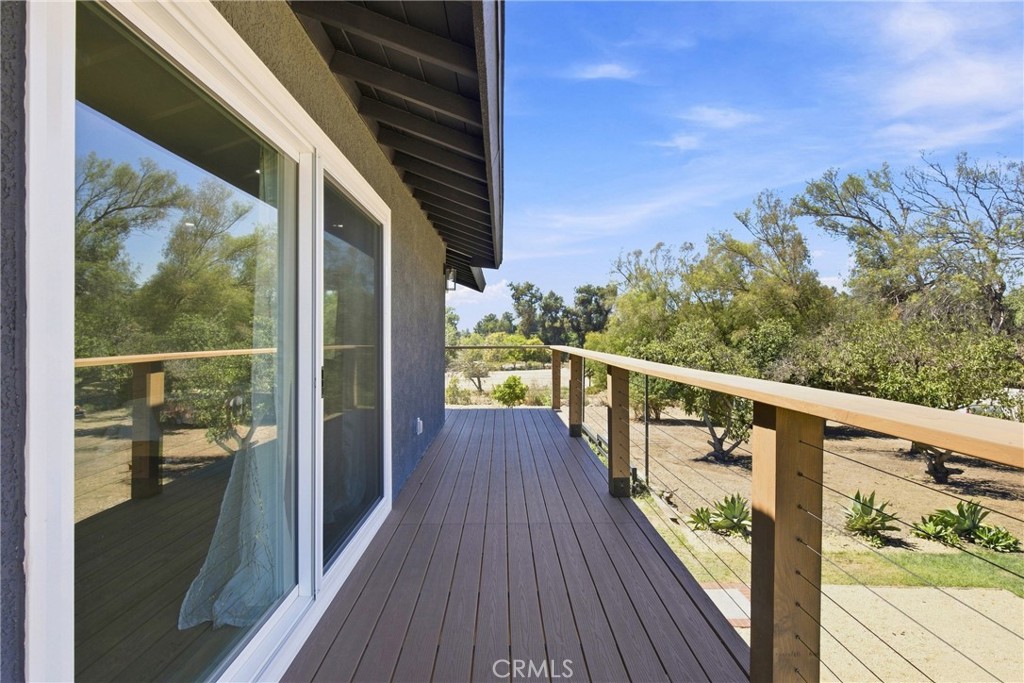 Raised wooden deck with cable railing overlooking a tree-dotted yard beside sliding glass doors.