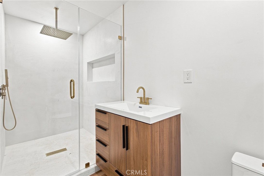 Modern bathroom with a glass walk-in shower and wood vanity with brass faucet.
