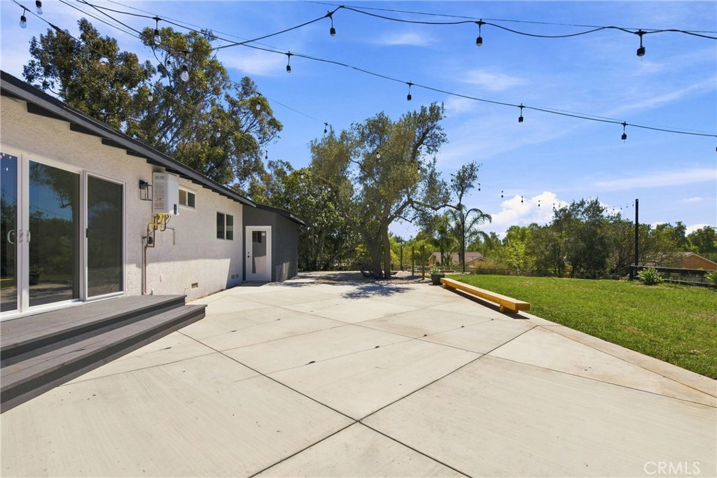 Backyard patio with a concrete terrace, wooden bench, lawn, and overhead string lights.