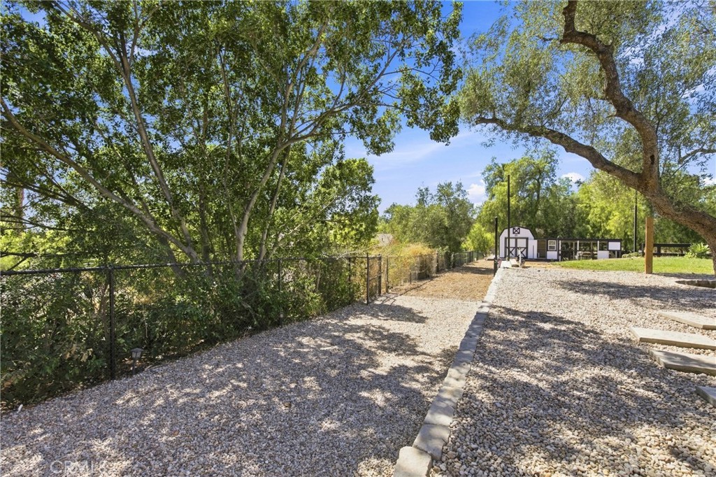 Gravel yard beneath mature trees, with a chain-link fence and small barn-like outbuilding.