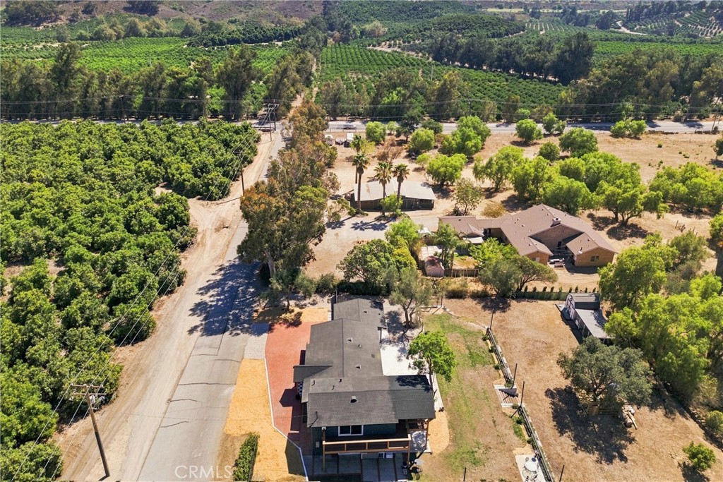 Aerial view of a rural home beside orchards, with dry grounds and hills in the distance.