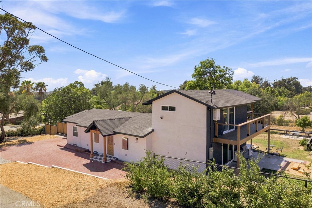 Two-story stucco home with a wooden deck and red-brick courtyard, viewed from above.