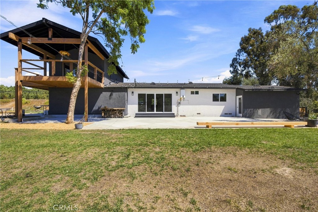 Rear of a modern home with a broad patio and elevated covered deck.