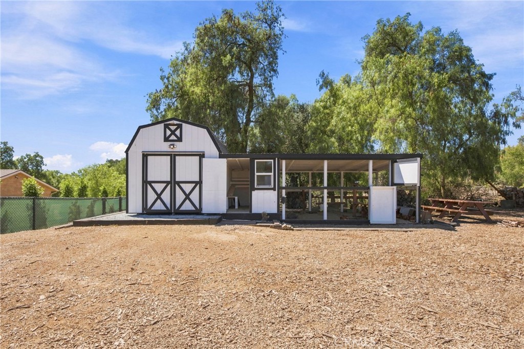 White barn-style outbuilding with black trim and an attached open-sided covered enclosure.