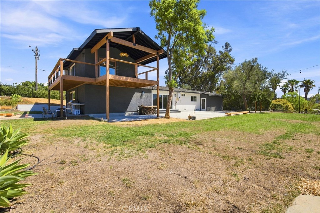 Modern home with an elevated wooden deck and covered balcony beside a broad yard.
