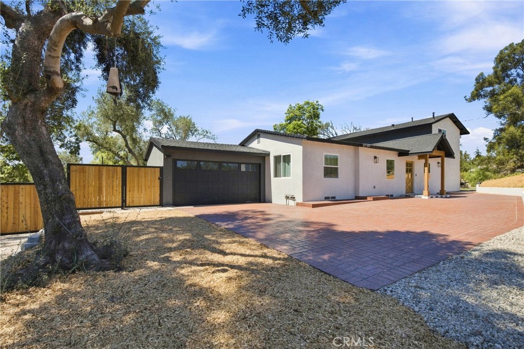 Single-story home with a broad red-paver driveway, dark garage door, and mature tree in front.