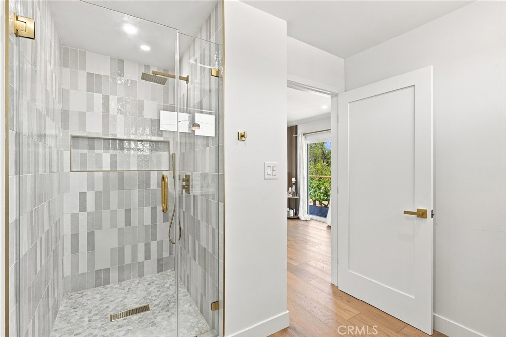 Bathroom with a glass walk-in shower, gray patterned tile, pebble floor, and brass fixtures.