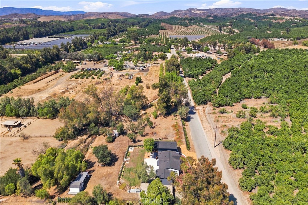 Aerial view of a rural home beside orchards, open land, and distant hills.