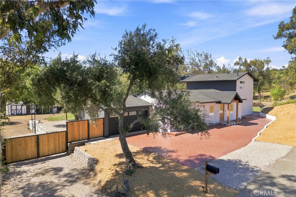 Two-story home with a wide brick driveway, wood fencing, and mature trees.