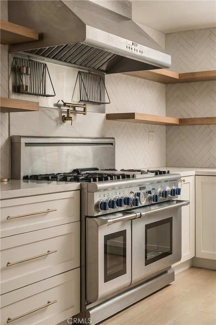 Kitchen with a stainless steel double-oven gas range, oversized hood, and open wood shelves.