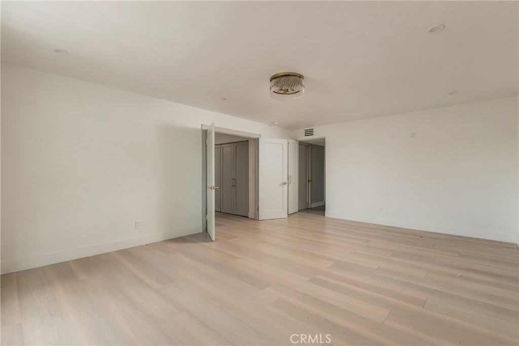 Vacant room with pale wood flooring, white walls, and open closet doors.