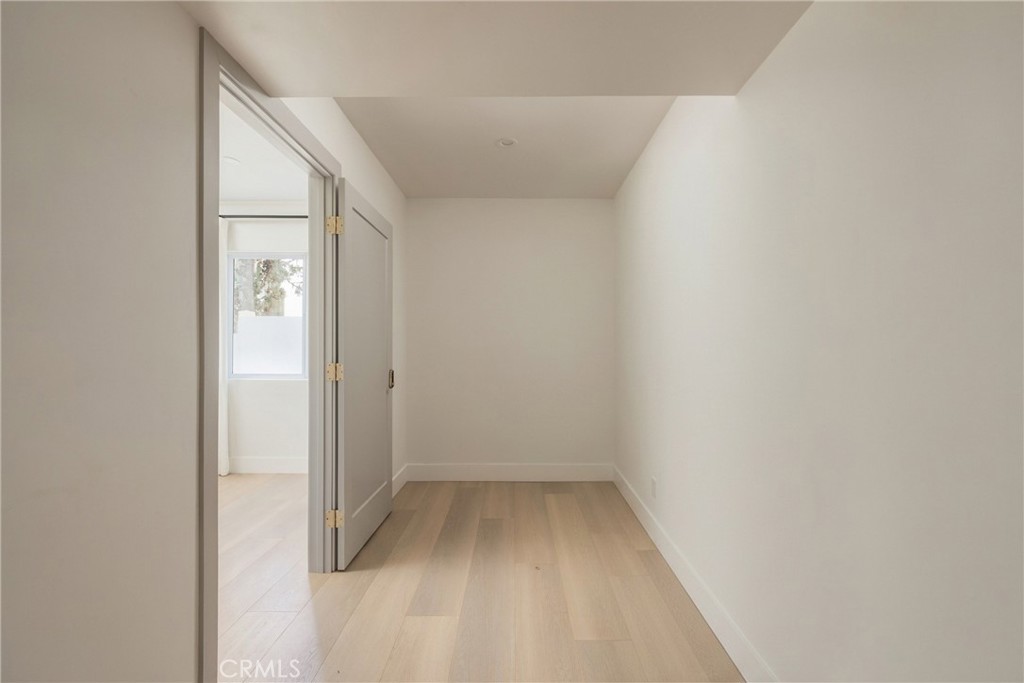 Empty narrow room with light wood flooring and an open door to a windowed adjoining space.