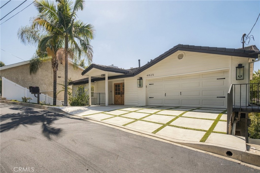 White single-story home with a two-car garage and grass-strip driveway beneath a tall palm tree.