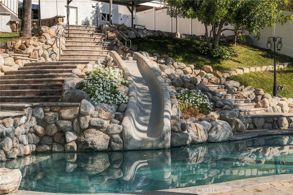 Swimming pool with a rock-lined waterslide, stone steps, and landscaped garden.