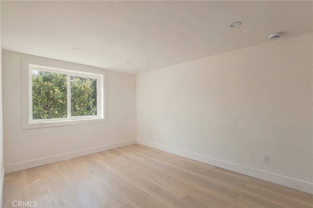 Empty room with light wood flooring and a wide window overlooking leafy trees.