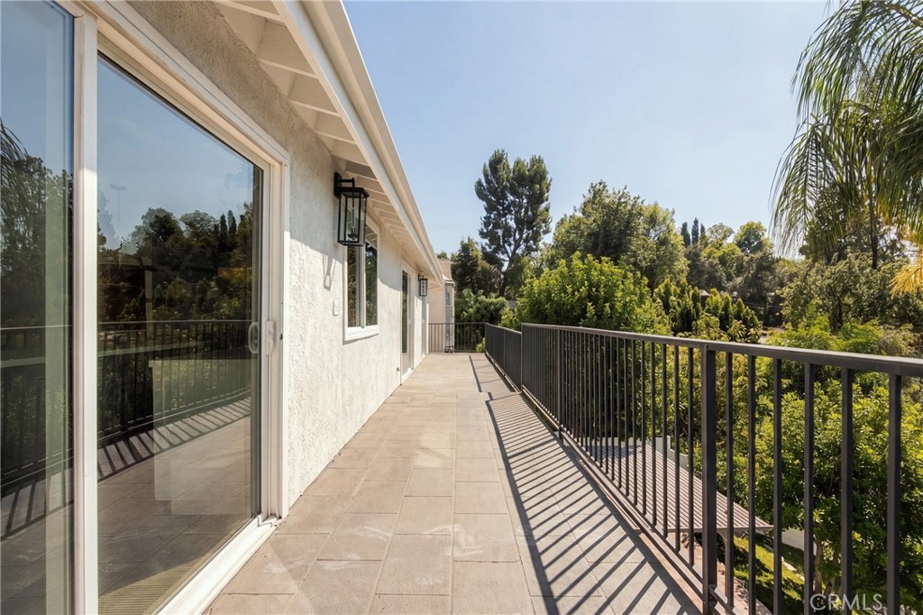 Tiled balcony with sliding glass doors, black railing, and leafy tree views.