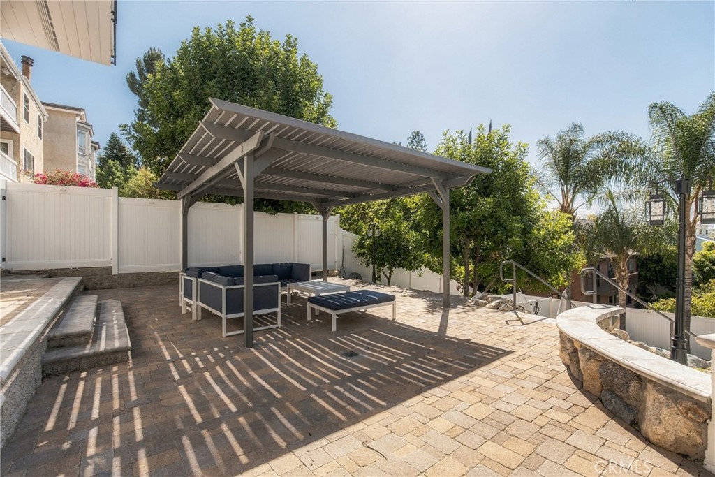 Paved patio with a metal pergola, cushioned seating, and steps beside a pool or spa.