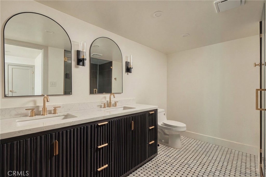 Bathroom with a dark double vanity, brass faucets, arched mirrors, and black-and-white mosaic flooring.