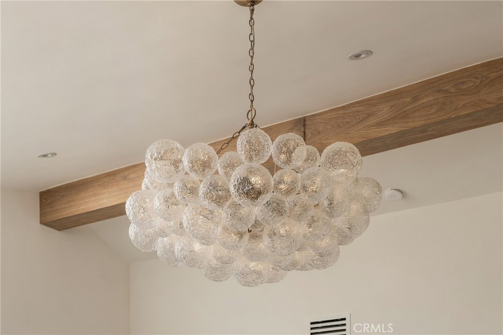 Clustered glass chandelier hanging beneath a wooden ceiling beam.