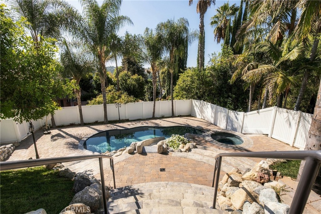 Backyard pool and circular spa surrounded by a paver patio, white fencing, and mature palms.