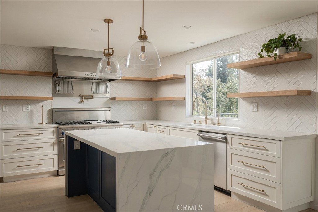 White kitchen with a marble-veined island, herringbone tile backsplash, and open wood shelves.