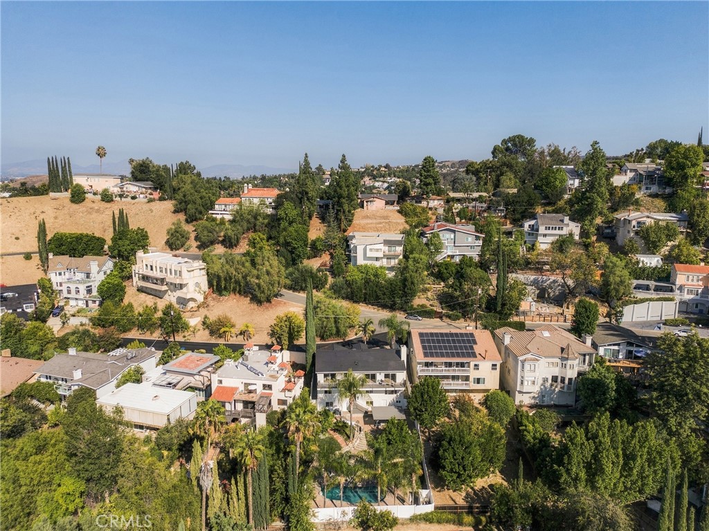 Aerial view of hillside homes among mature trees, with a swimming pool and rooftop solar panels.