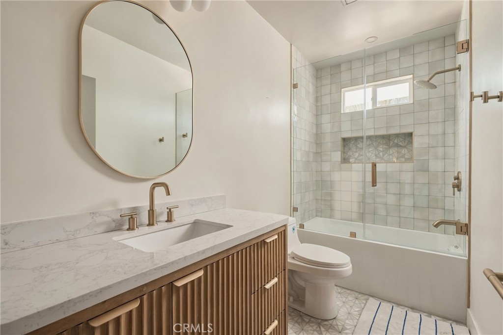 Bathroom with a fluted wood vanity and glass-enclosed tiled tub-shower.