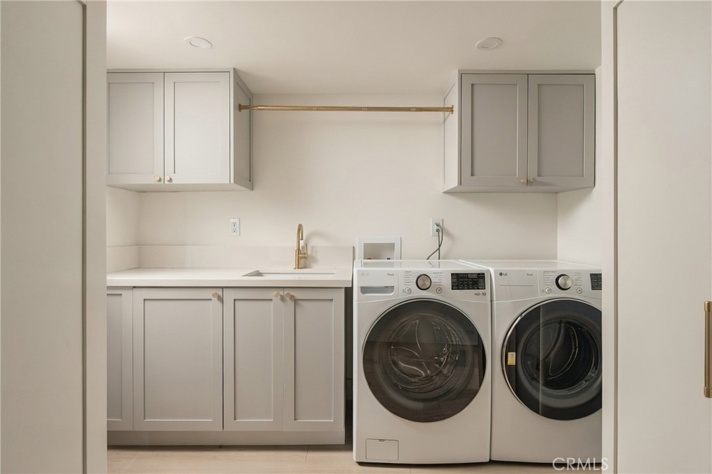 Laundry room with white cabinets, sink, and side-by-side front-loading washer and dryer.