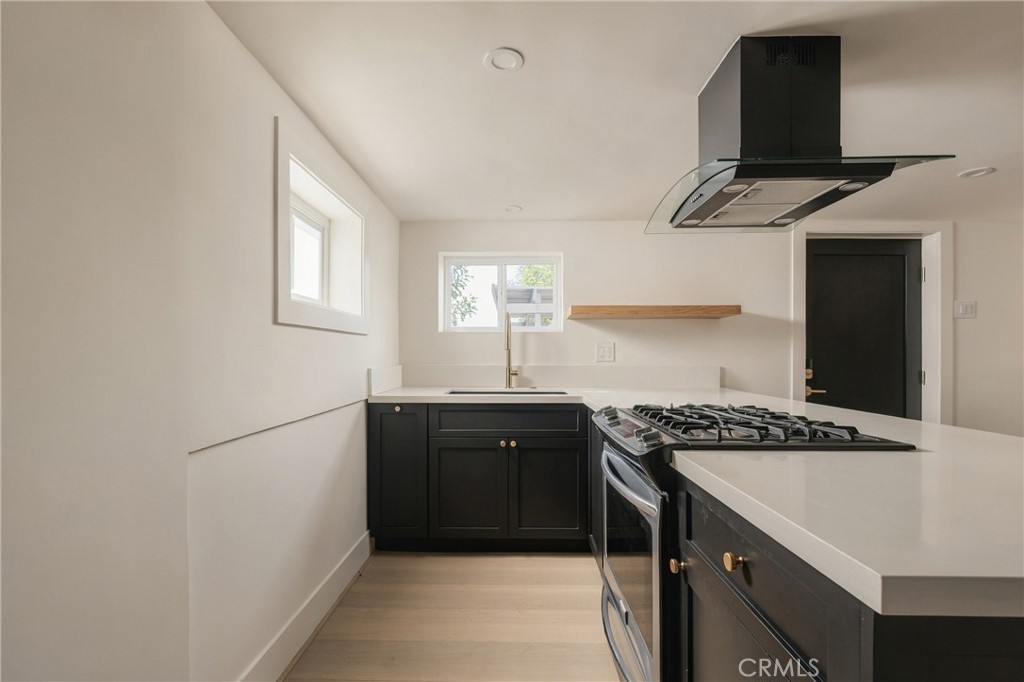 Modern kitchen with black cabinets, white counters, and a gas cooktop on a large peninsula.