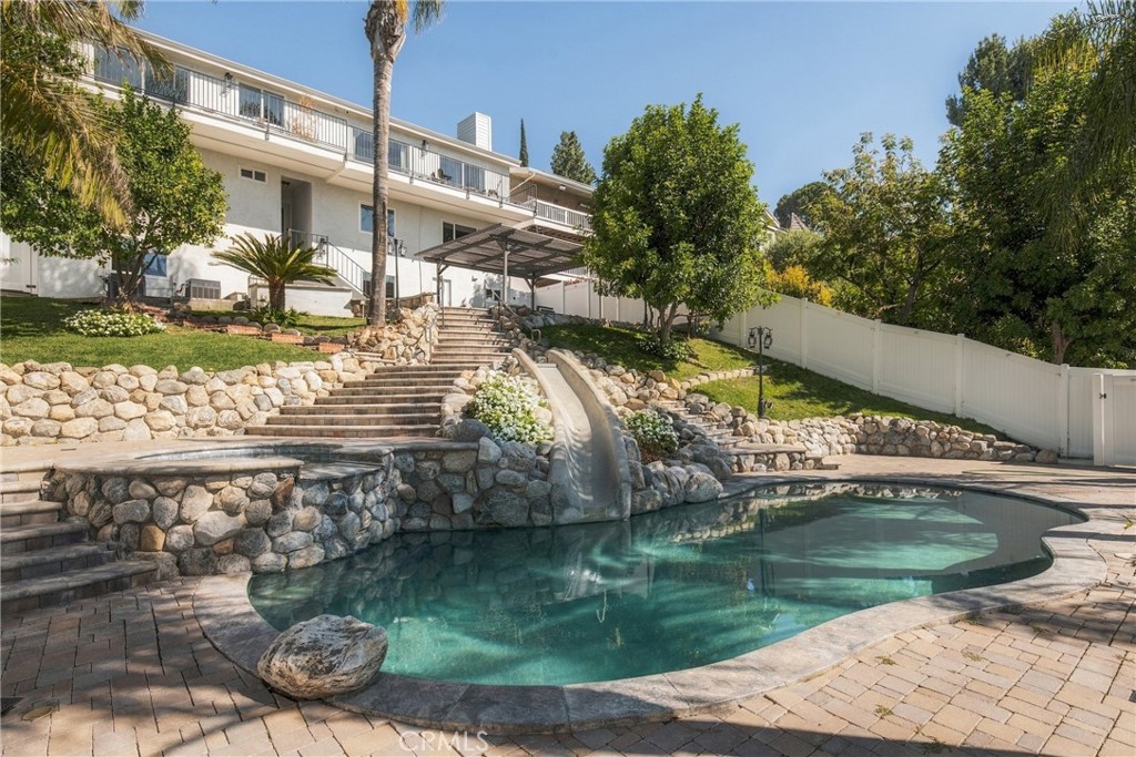 Backyard pool with a stone waterfall, tiered steps, and landscaped patio.