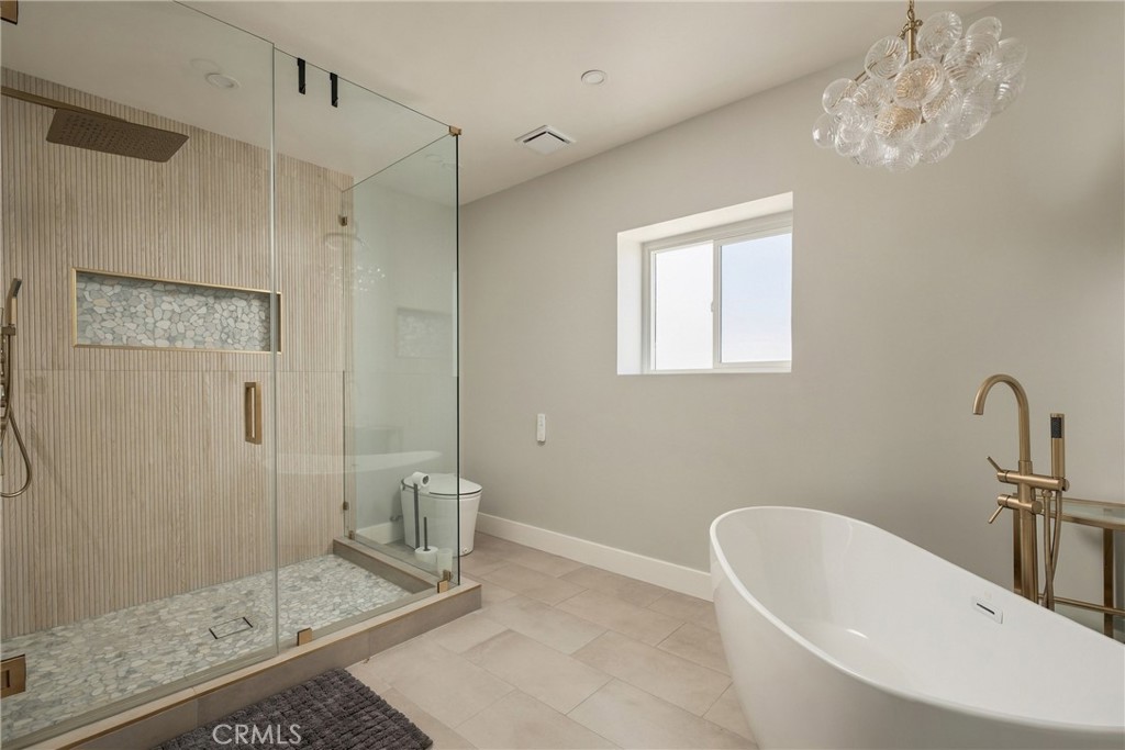 Modern bathroom with a pebble-floor glass shower, freestanding tub, and brass fixtures.