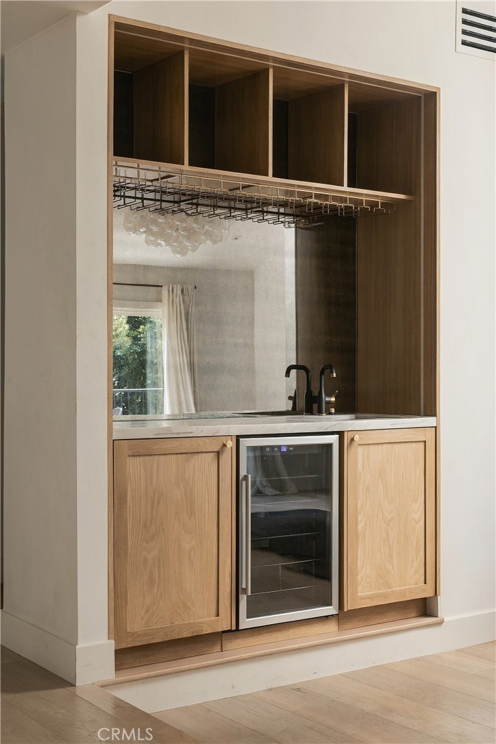 Built-in wet bar with oak cabinetry, a sink, glass rack, and under-counter wine refrigerator.