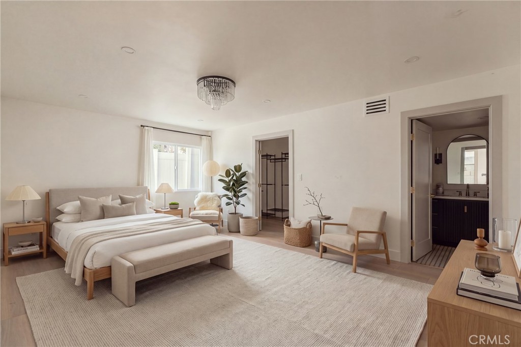 Staged bedroom with a large neutral bed, light rug, and doorway to a bathroom.