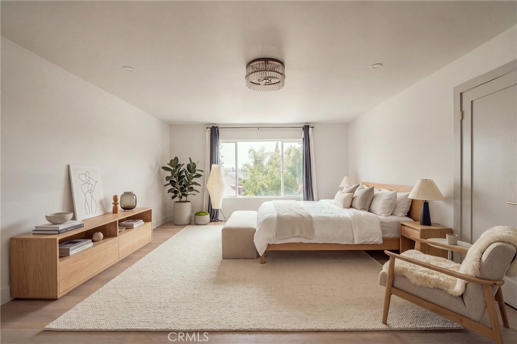 Staged bedroom with a white bed, light wood dresser, and window overlooking trees.