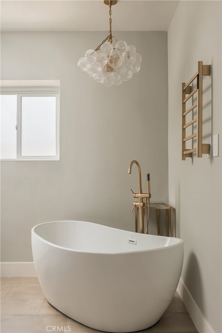 Freestanding bathtub beneath a glass globe chandelier, with brushed brass fixtures and a wall-mounted towel warmer.
