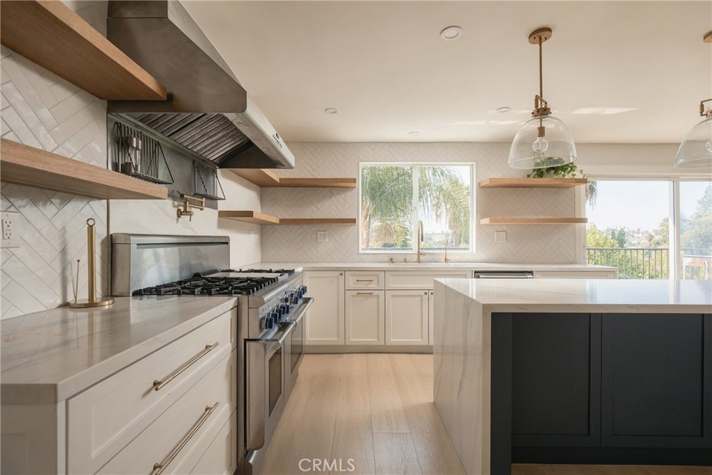 Modern kitchen with a marble island, white cabinetry, brass fixtures, and a stainless steel range.