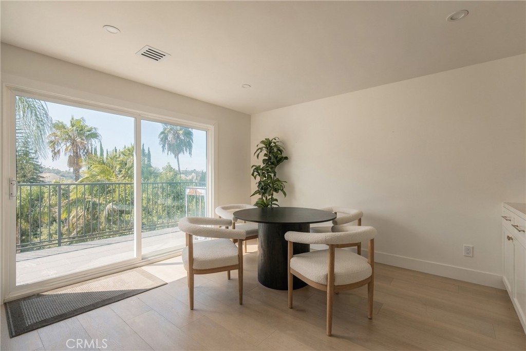 Dining area with a round black table beside sliding glass doors opening to a palm-lined balcony.
